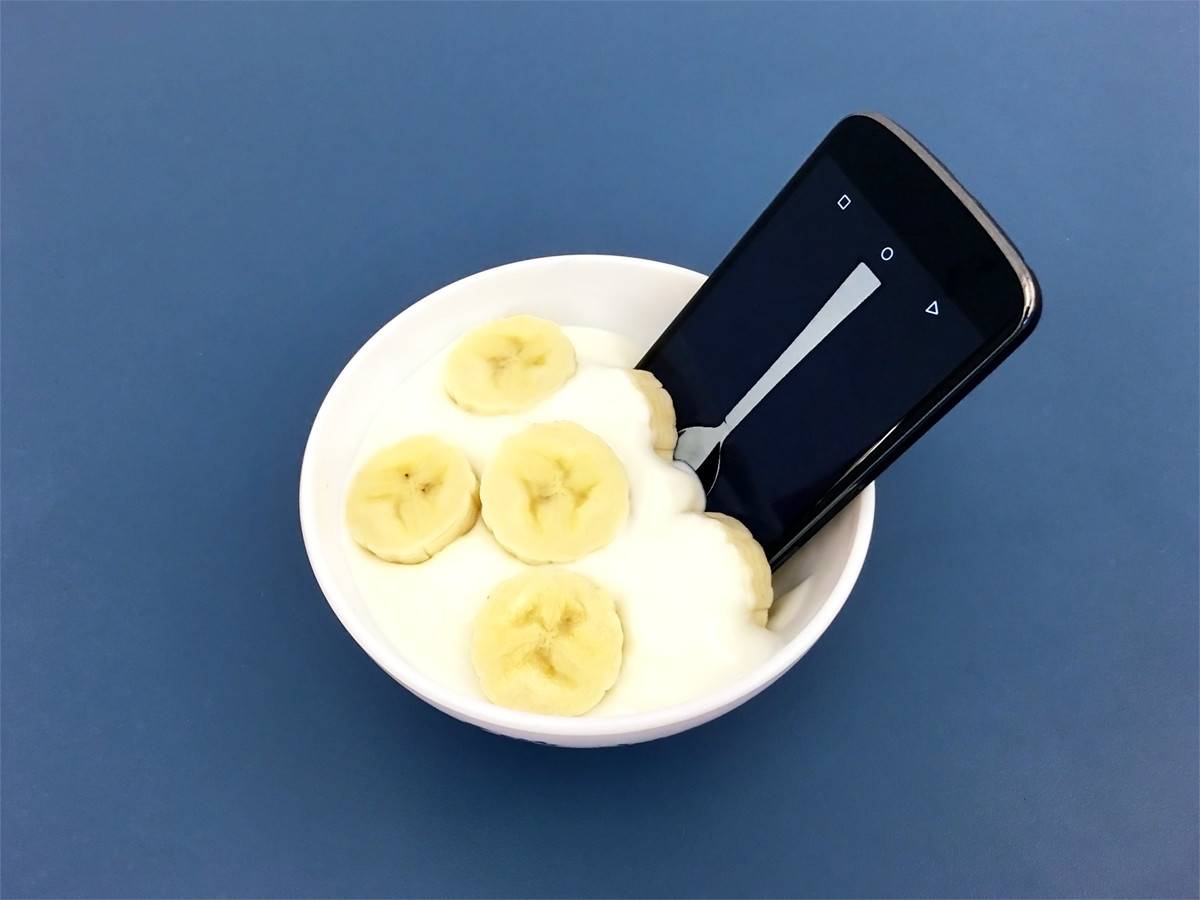 A phone used as a spoon in a bowl of yogurt and banana slices